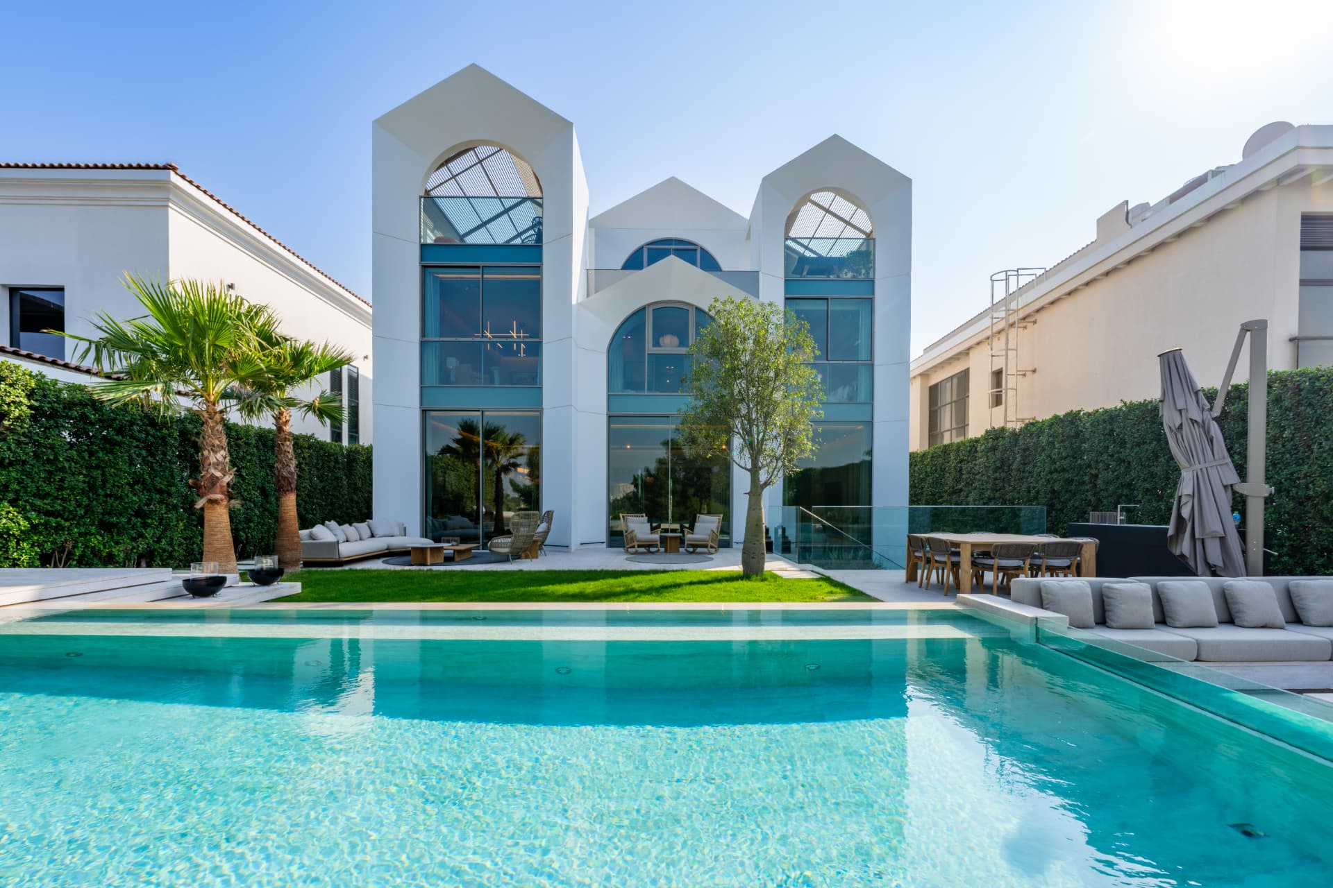 K47 pool and lawn by day facing the arched glazed facade with palms and outdoor dining