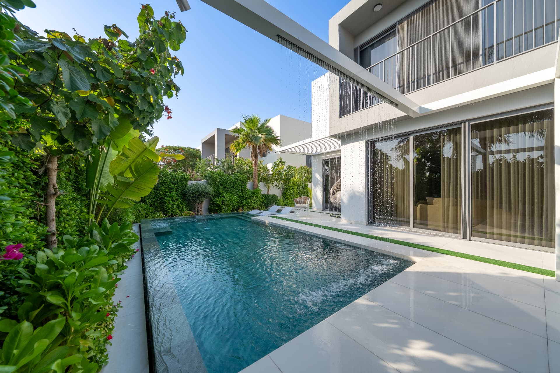 Villa 41 by day — rain-water curtain falling from the pergola beam beside the lap pool and terrace