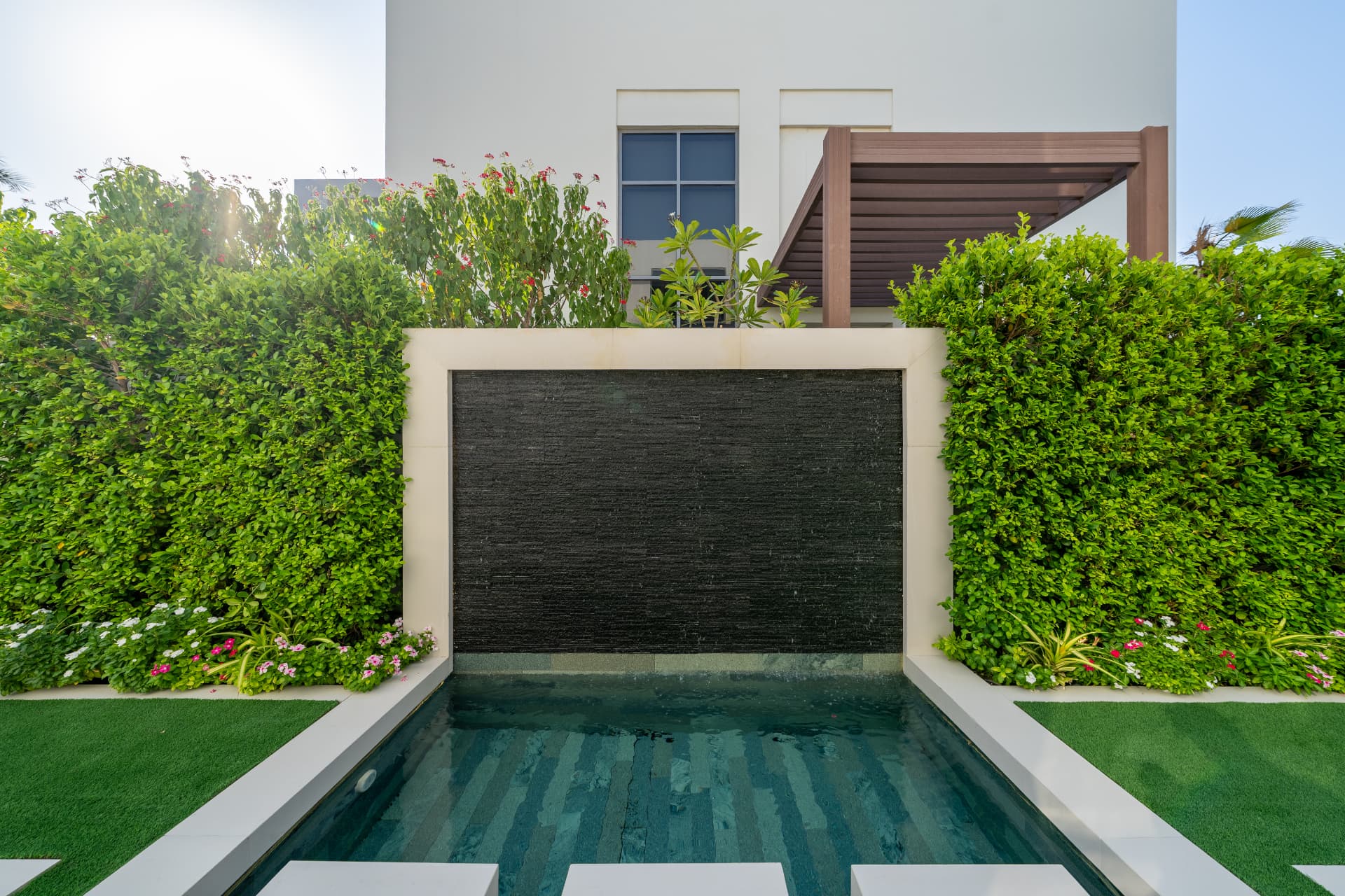 Villa 41 bespoke stone waterfall wall by day, flanked by clipped hedges above a shallow reflecting pool