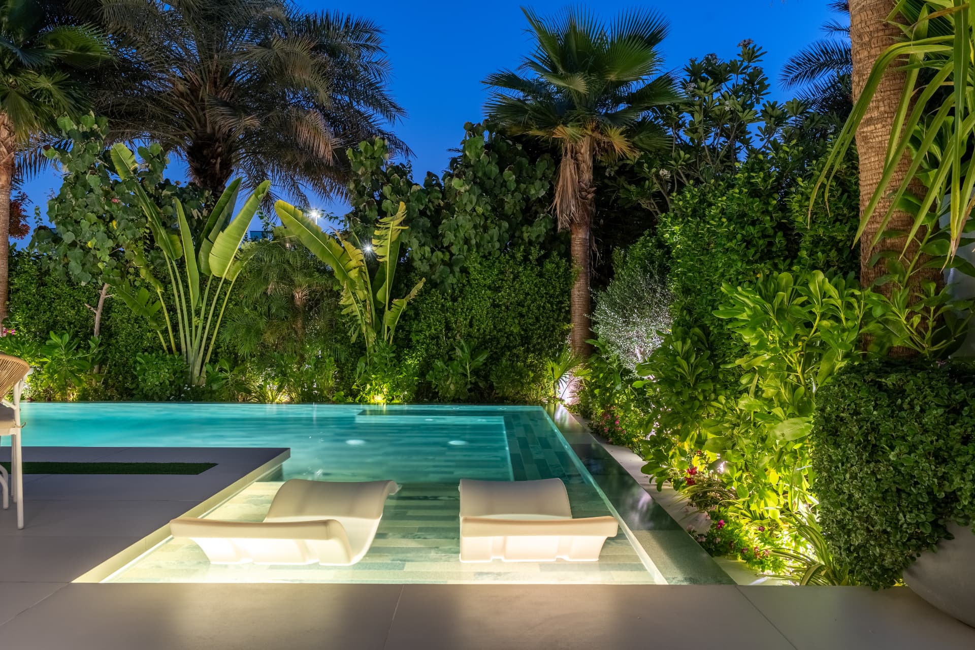 Villa 41 sun-shelf loungers lit from below, framed by uplit palms and shrubs at night