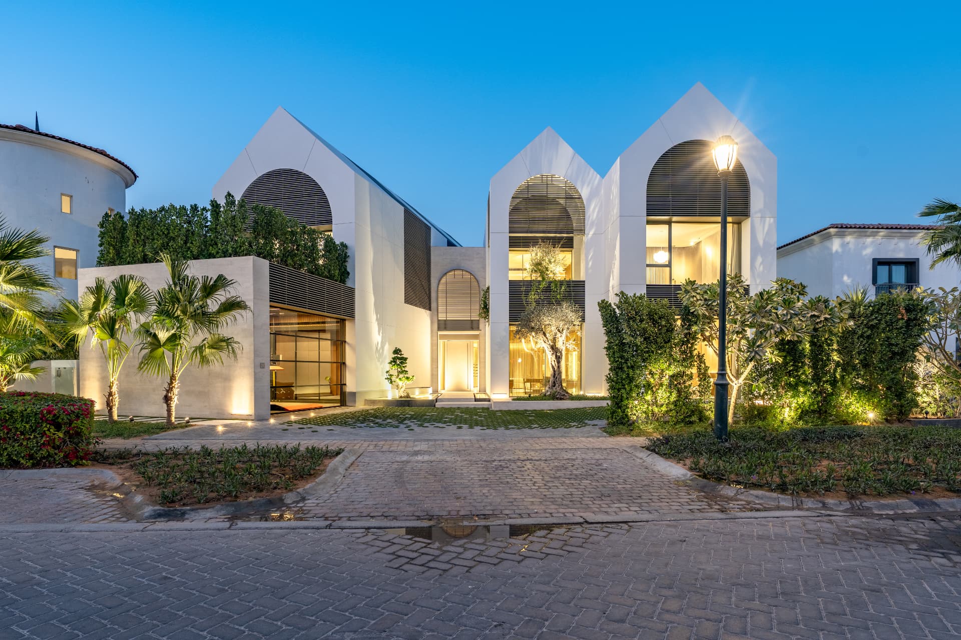 K82 in Wildflower — three arched gable volumes with louvred screens and mature olive tree at dusk
