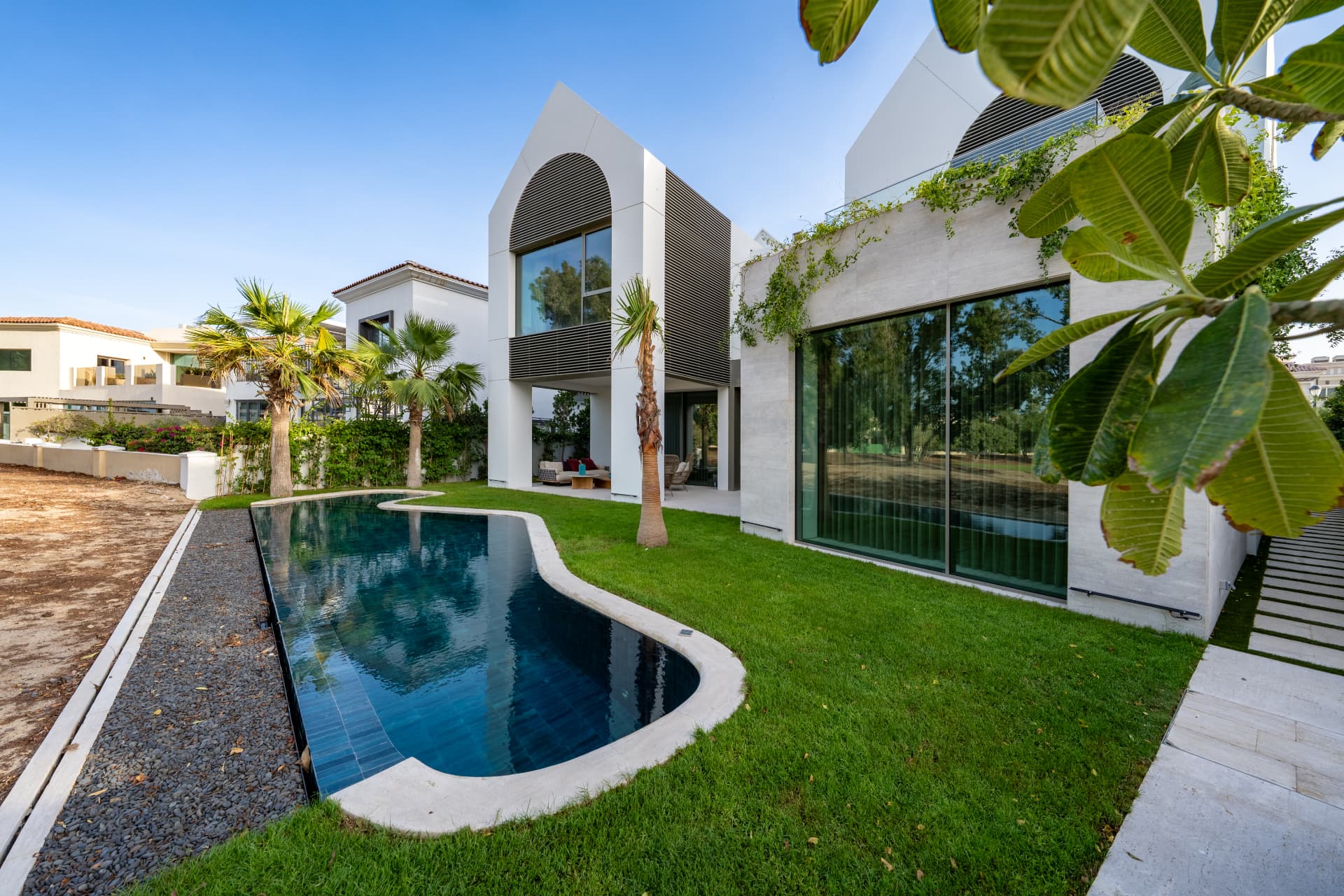 K82 garden view with curved pool, lawn, palms and the travertine-clad extension by day