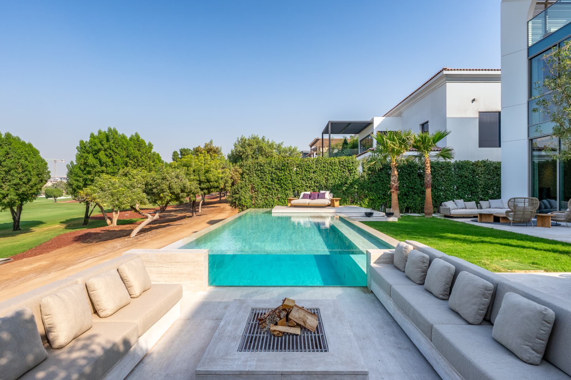 K47 rear garden by day — glass-edge pool, travertine fire pit and lawn opening onto the golf course