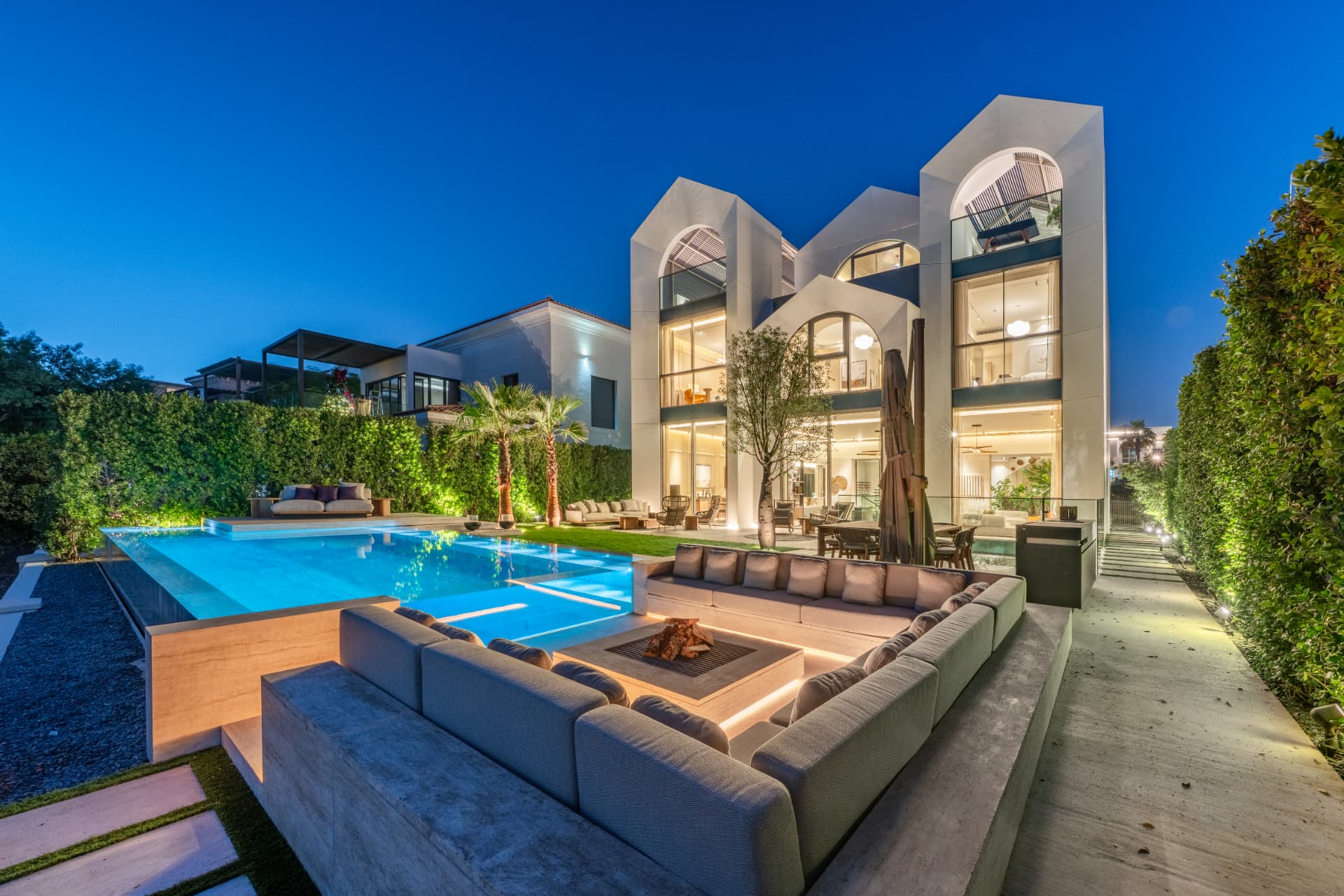 K47 in Wildflower, Jumeirah Golf Estates — arched villa façade and infinity pool with sunken fire-pit lounge at dusk