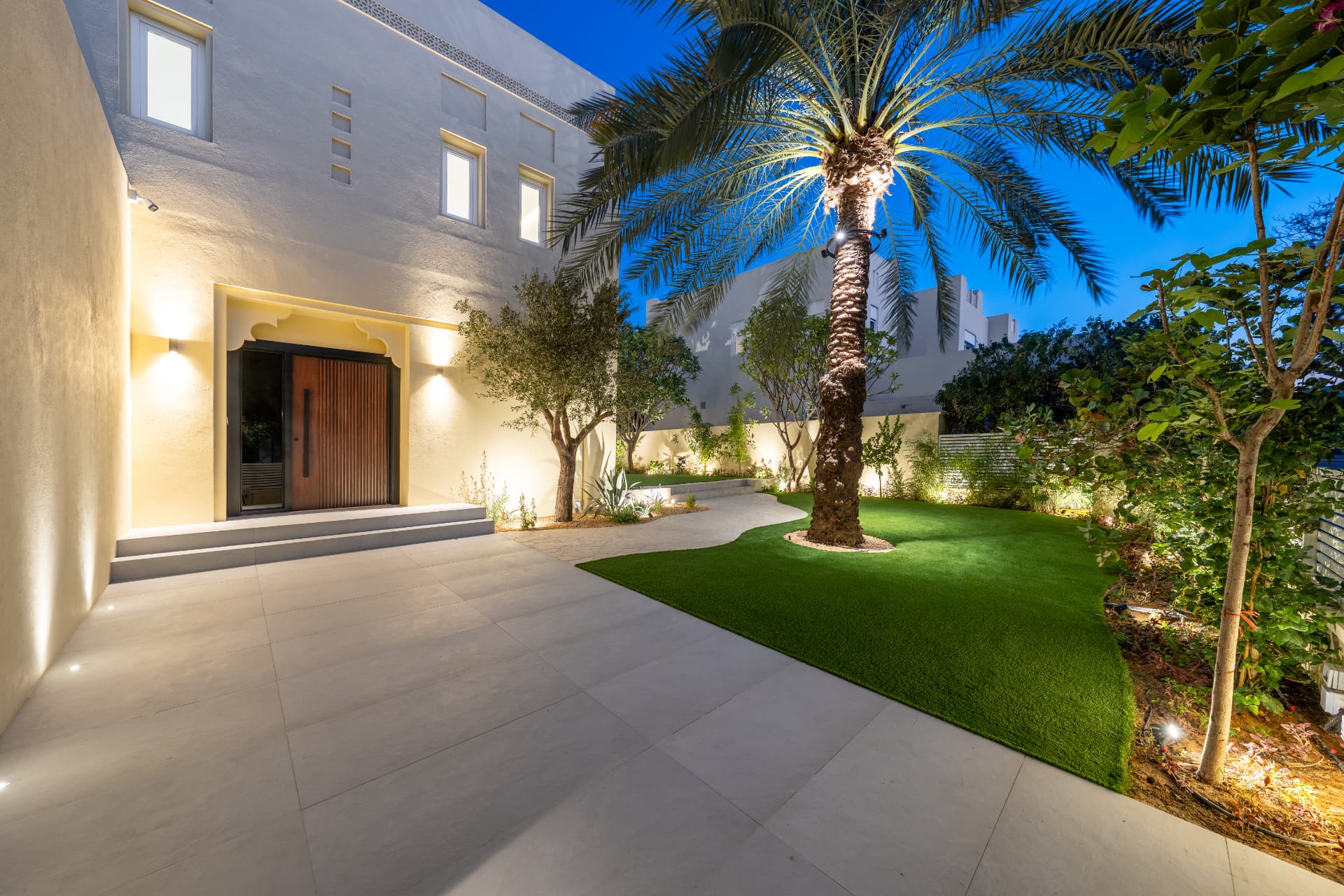 Villa 55 entrance courtyard at night with timber door, uplit palm and curved lawn