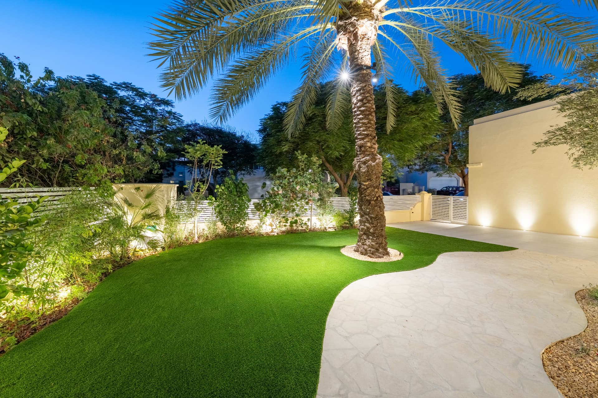 Villa 55 — gebogen gazon rond de uitgelichte dadelpalm met flagstone-pad naar de oprit bij blauw uur