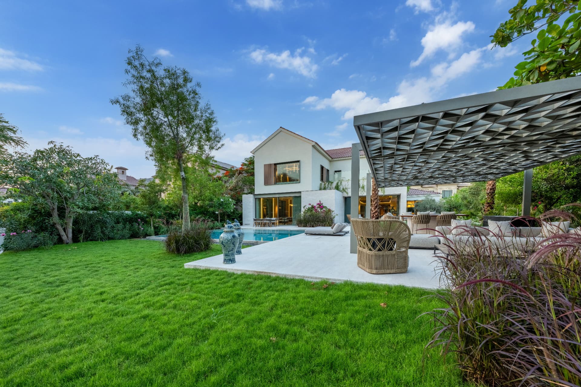 C51 — lawn and garden at dusk with the lit villa, pool and pergola lounge