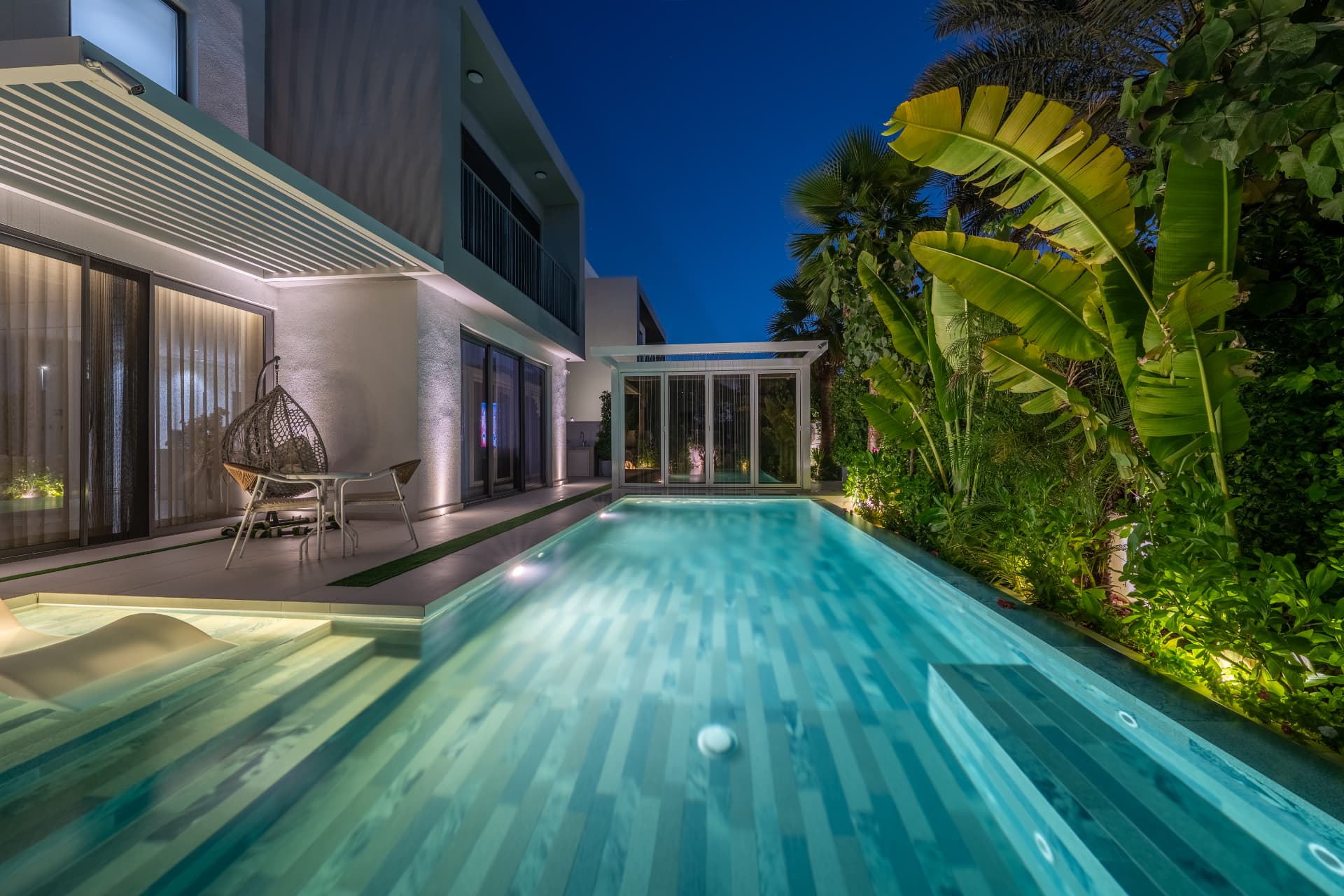 Villa 41 at night — lap pool leading to the glazed garden room beneath the rain curtain