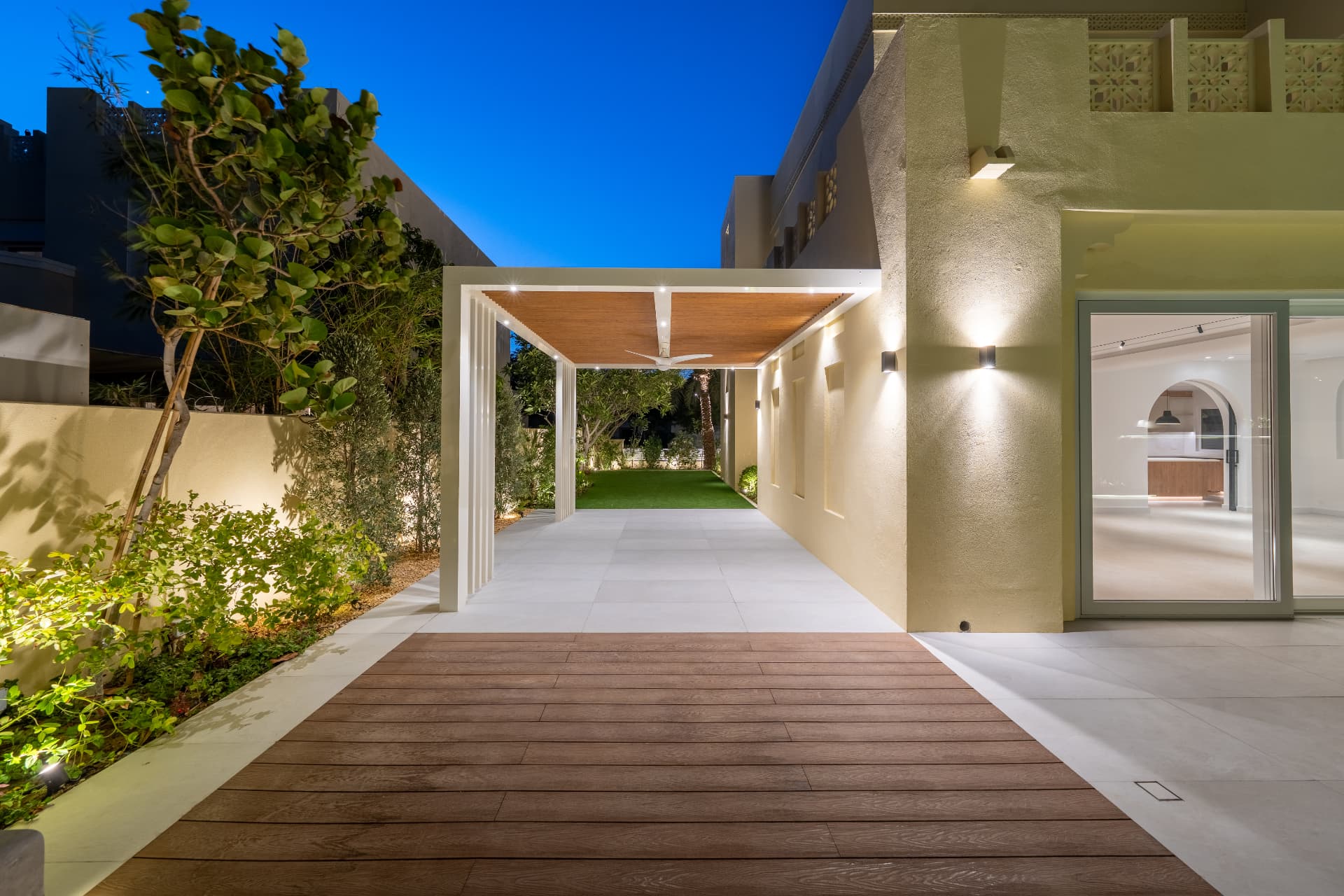 Villa 55 — houten deck en verlichte pergola langs de villa met doorzicht naar het gazon bij avond
