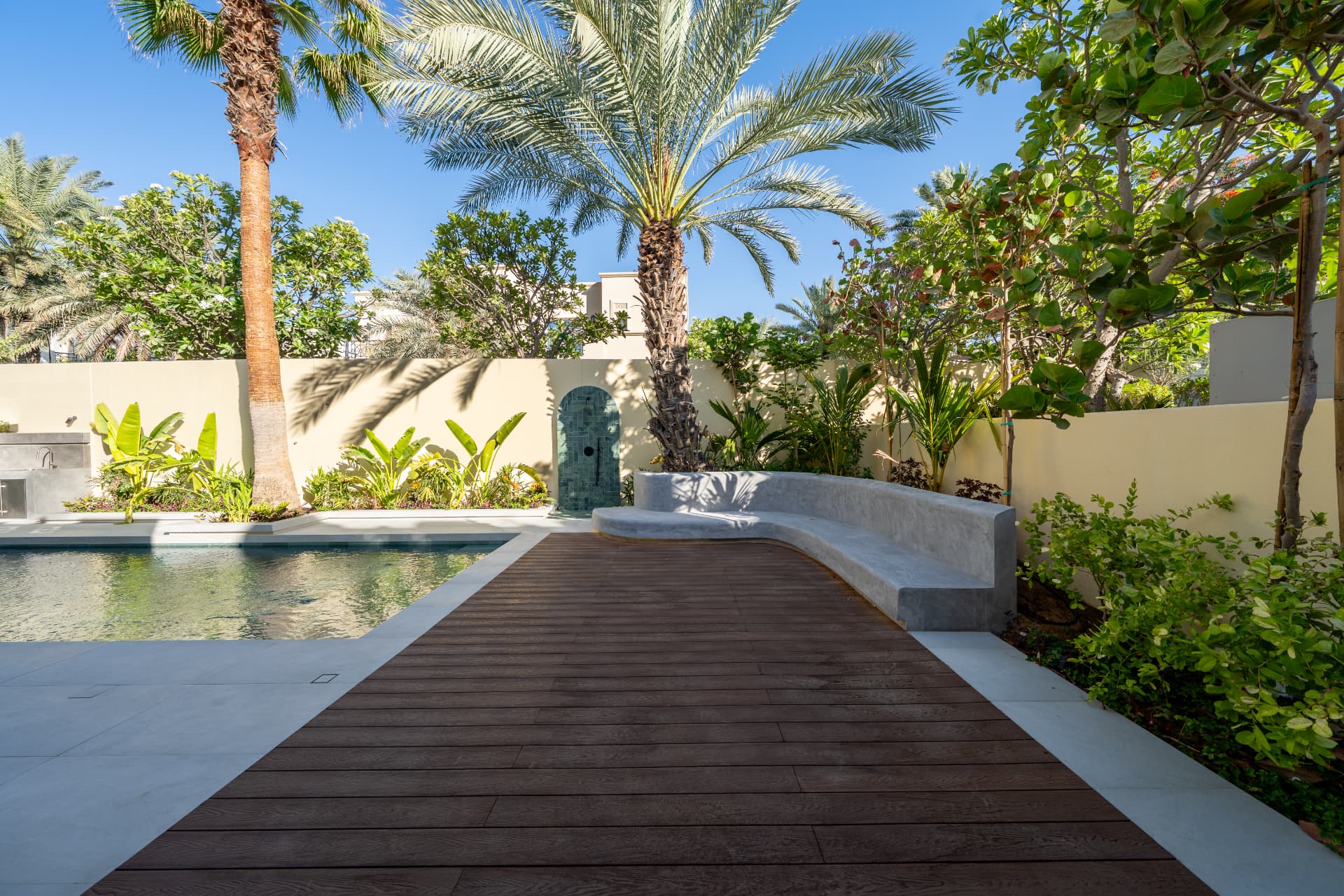 Villa 55 — houten deck naast het zwembad met gebogen betonnen bank en groene tegelnis overdag