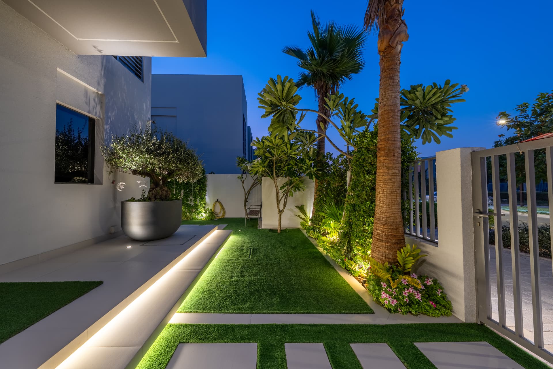 Villa 41 side entrance walkway at night — lit stepping pads, olive tree in a planter and uplit palms