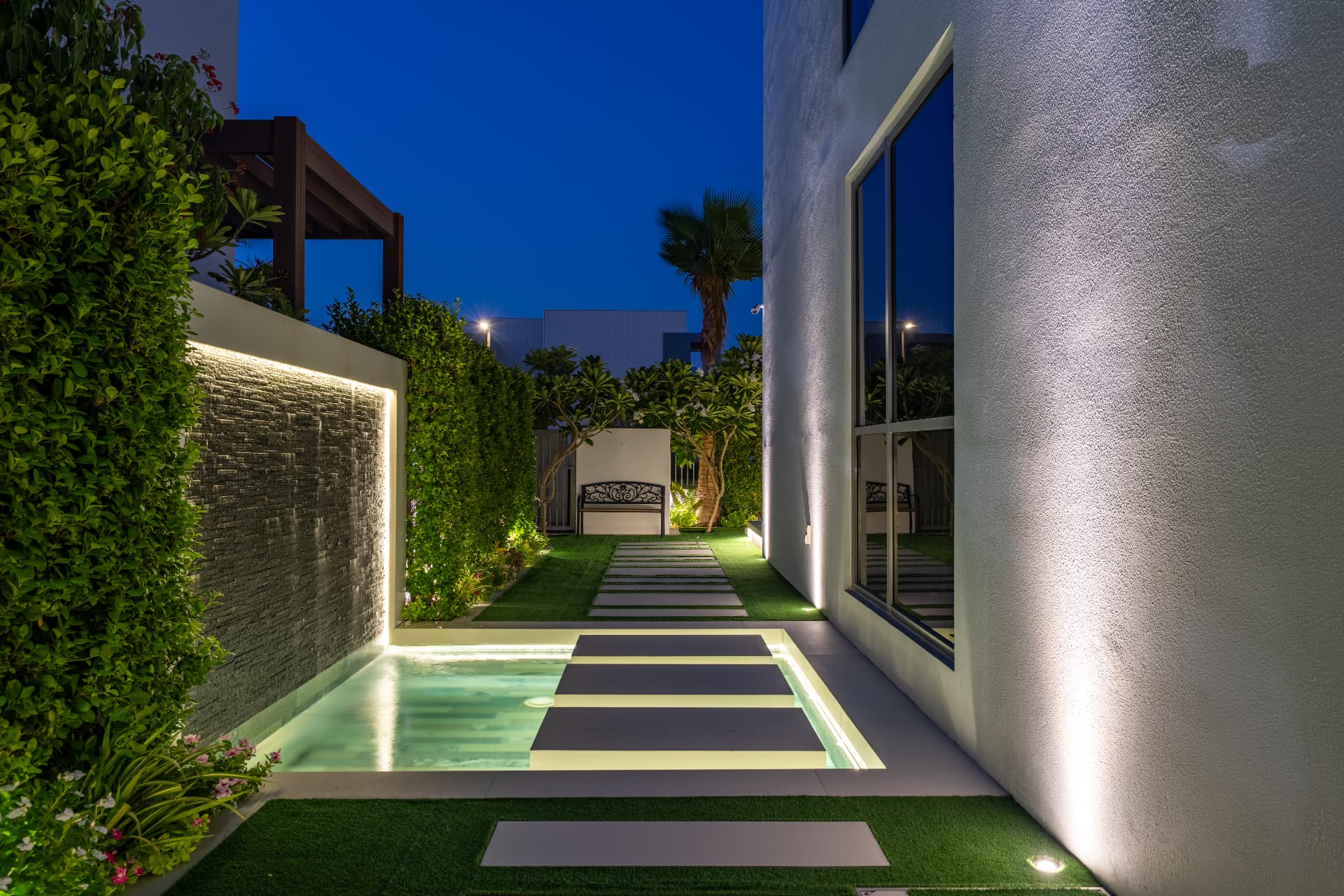 Villa 41 courtyard at night — illuminated waterfall wall, stepping pads across the water and lit walkway