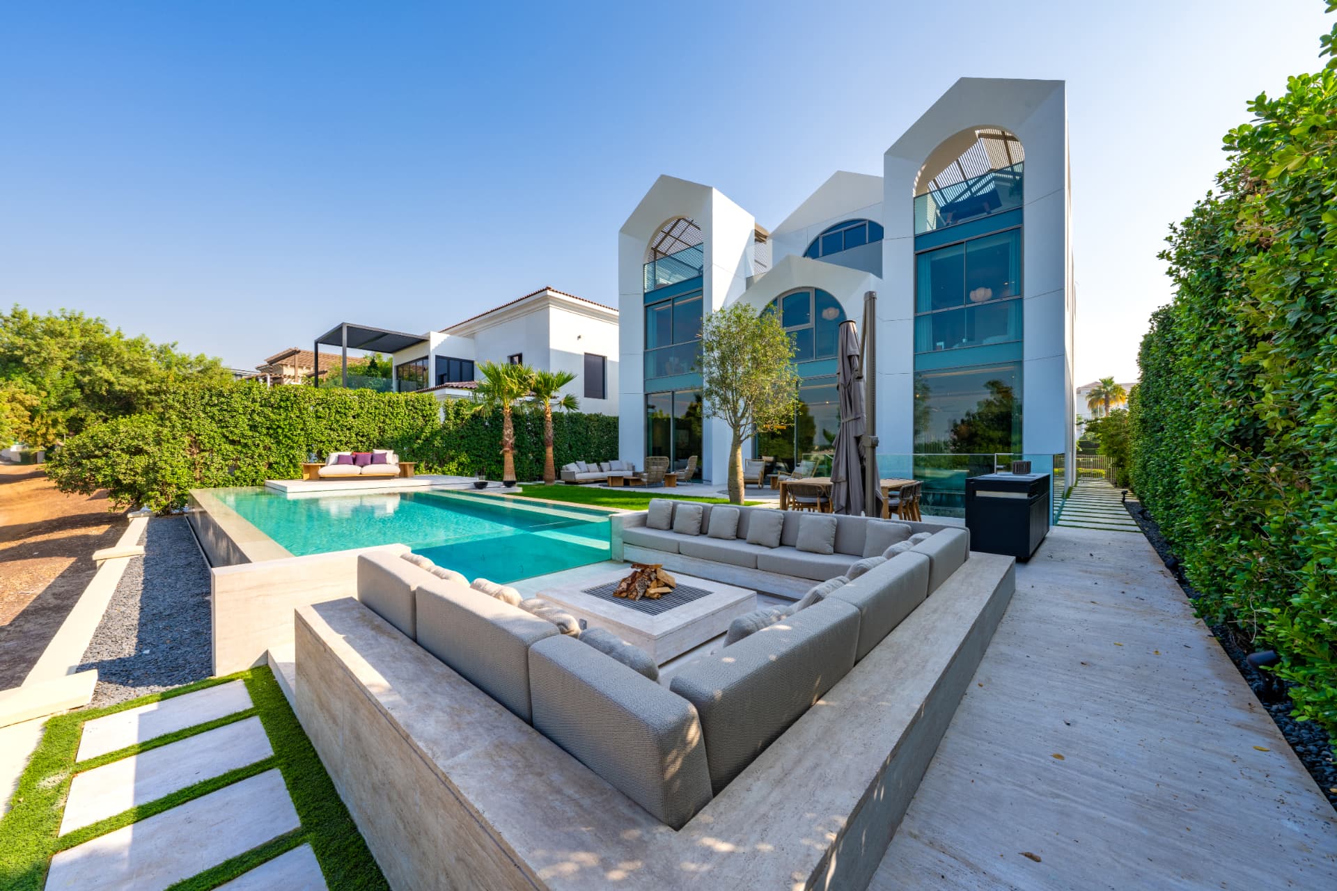 K47 sunken seating and fire table beside the glass-edge pool by day, with paved walkway and hedging