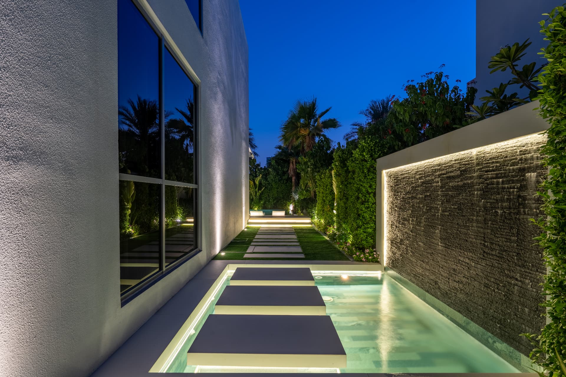 Villa 41 side courtyard at night — stone water wall, stepping pads over a shallow pool and lawn joints