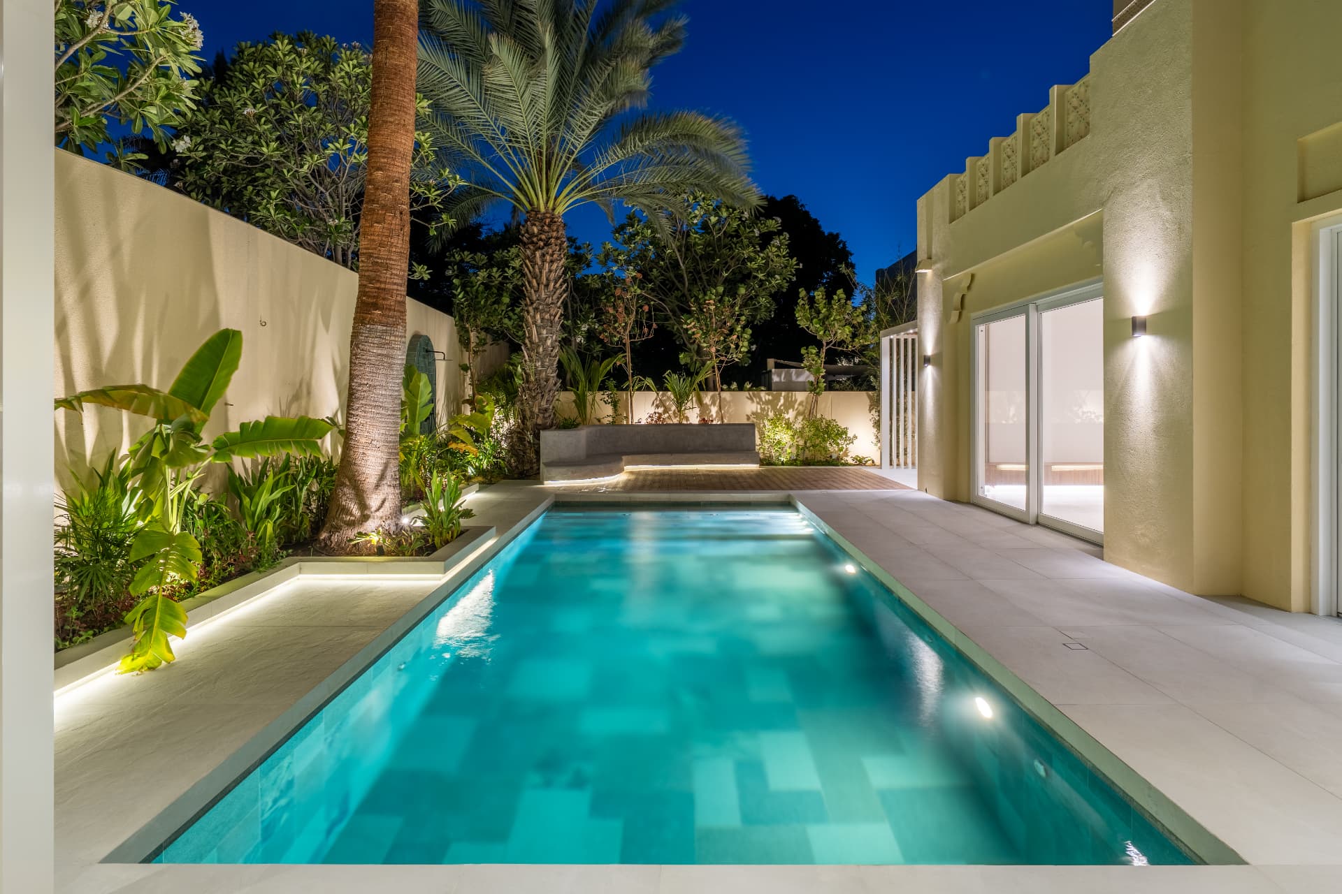 Villa 55 in Al Mahra — lap pool lit at night between planted beds and a date palm