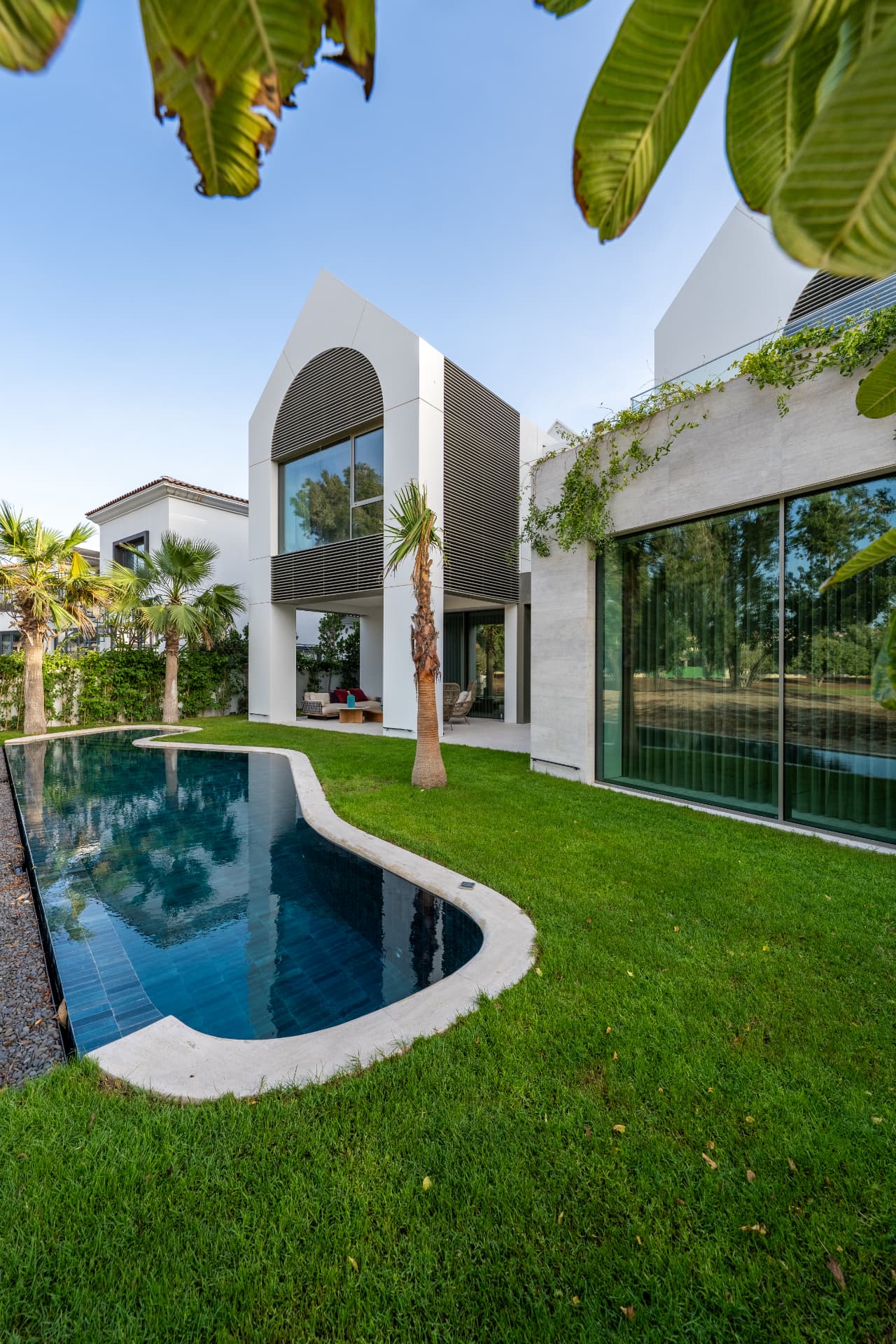 K82 garden with curved dark-tiled pool, lawn and travertine-clad extension with full-height glazing