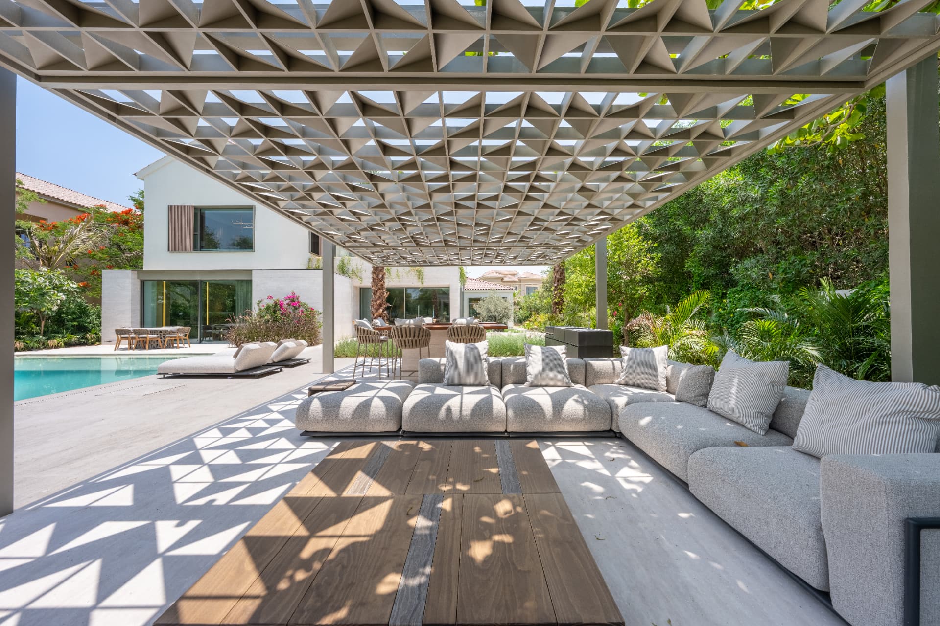 C51 — shaded lounge under the patterned pergola canopy, with pool and villa beyond