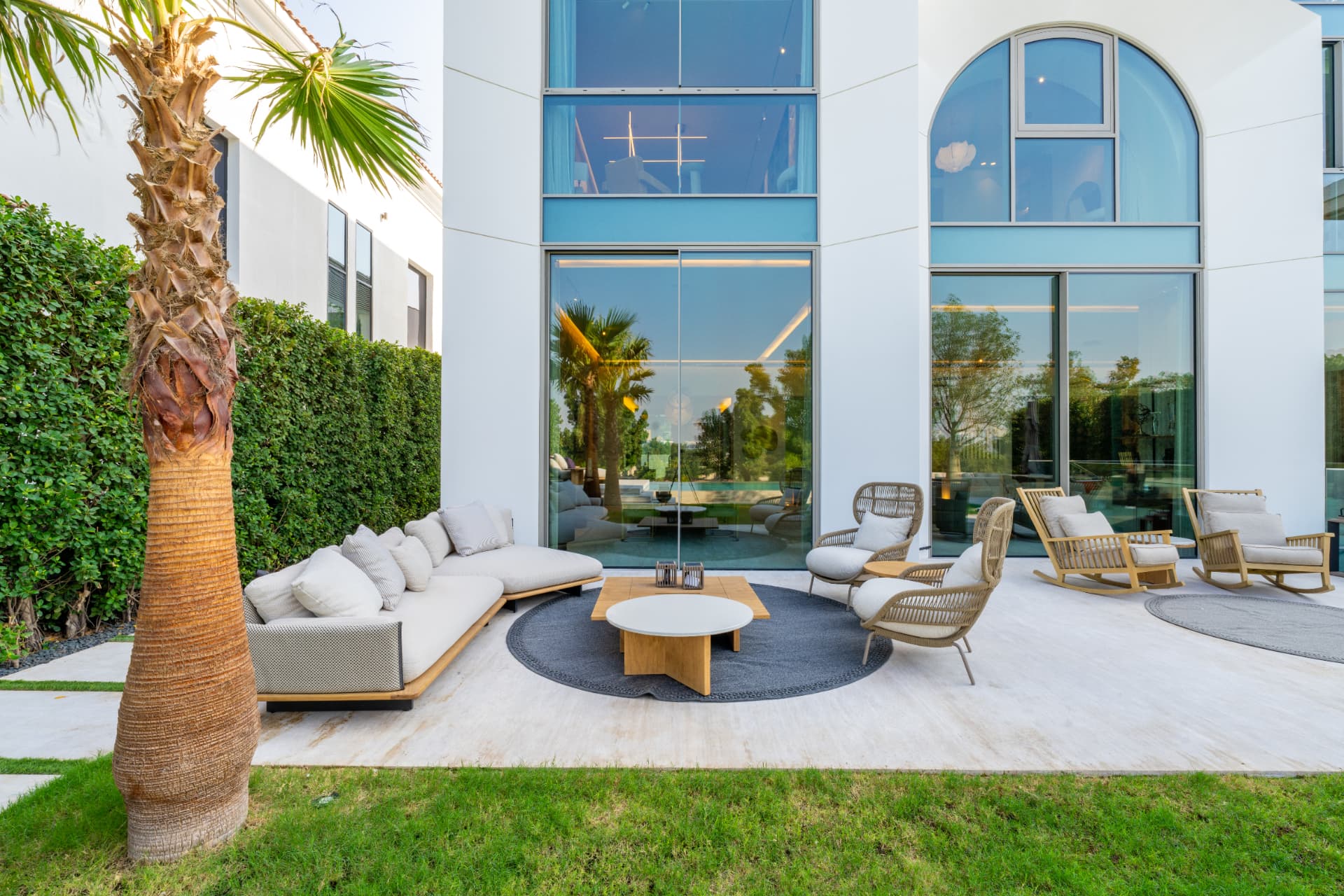 K47 shaded terrace with low seating, rattan chairs and a palm against the full-height glazing