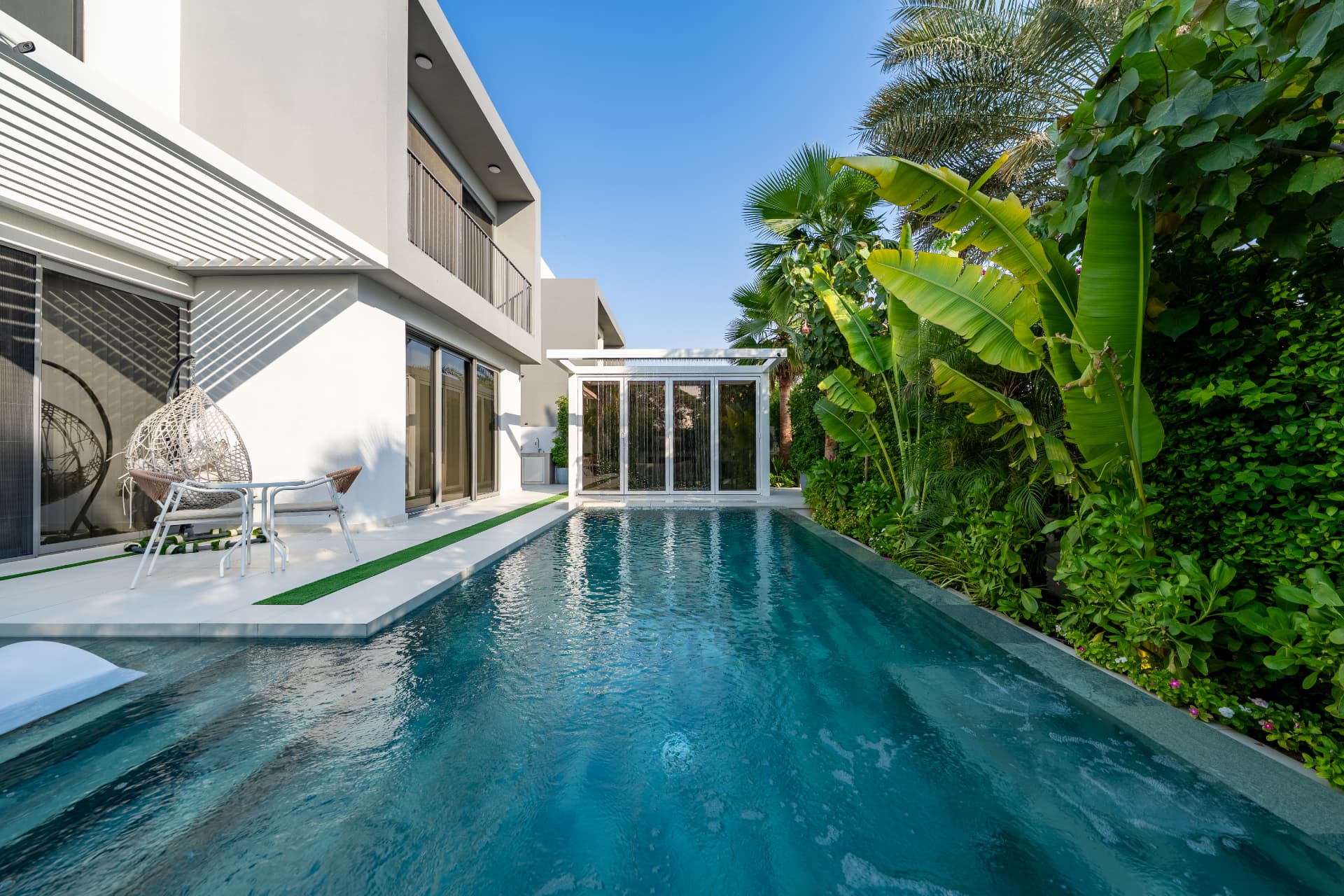 Villa 41 lap pool by day running toward the glass garden room, with terrace seating and banana plants